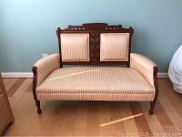 Front view of antique carved wood settee sofa with cream and beige striped upholstery on wooden floor.