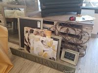 Photo showing group of canvas art pieces with floral and succulent prints, wooden shelf with 'Give Thanks' lettering, metal wall hanging and some frames leaning on a piece of furniture.