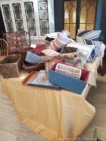 Overview of table with various baskets, pillows, linens, and trays packed and stacked together