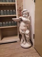 Full view of the 38 inch tall cherub statue showing the figure standing with a tray in hand against a wall corner.