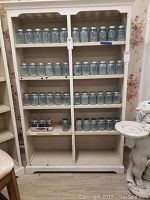 Full front view of white painted wooden bookshelf with four shelf surfaces and decorative scalloped crown molding
