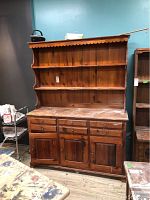 Front view of a large wooden country-style hutch with three drawers and three cabinet doors below, topped with two shelves and scalloped trim.