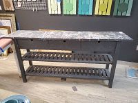 Front view of wooden work bench showing two drawers and two slatted lower shelves with black paint and paint splatter on top