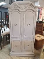 Front view showing the ornate carved top cornice, recessed panel doors, and ring pulls on all four doors.