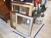 Two framed mirrors, one with ornate white frame, some marks and scratches visible. Several window pane frames stacked behind mirrors, part of wooden furniture and other items adjacent.