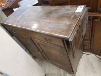 Wooden bar table with dark finish showing scratches and marks on the top surface and closed drop leaves down the side.