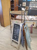 Three wooden folding chairs leaning against the metal storage rack and the chalkboard sign, showing scratches and marks on the chairs.