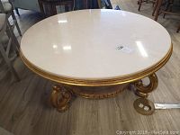 Front view of round ivory tone marble top coffee table with gold painted ornate base.