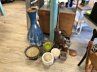 Photo showing the large blue floor vase, decorative footed bowl, multiple small planter pots, copper pail, copper coffee pot, lids, and canes grouped together on floor.