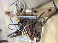 Wooden ox yoke with two curved metal horns and plastic container filled with leather horse tack items.