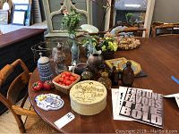 Overview photo showing all items including vases, ceramic figurines, bottles, tin, flowers, and prints on a wooden table.