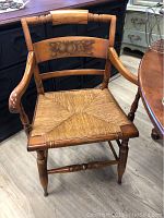 Front view of a captain's chair showing painted fruit motif on backrest and woven rush seat