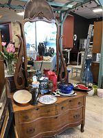 Full size view of wooden dresser with attached ornate mirror and assortment of pottery and decorative items on top.