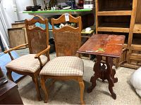 Two wooden cane back chairs with upholstered seats and a wooden side table with visible paint stains. Chairs include one captain's chair with armrests and one regular chair, both showing used condition with some stains.