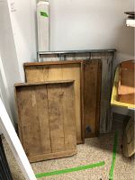 Four vintage wooden dough or bread boards stacked against a wall. Boards vary in size and finish with signs of wear.