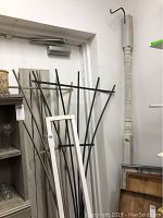 Photo of black metal yard hook, tall with curved hook top, standing upright with white wood trellis behind it.