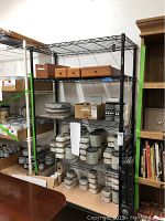 Full view of the black metal wire shelf rack with multiple wire shelves holding various jars and boxes.