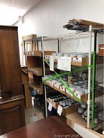 White and black metal wire utility shelving units loaded with small boxes and paint cans for storage. Shows shelving condition and details.