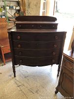 Front view of antique chest of drawers showing curved drawer fronts, four large drawers, two smaller top drawers, turned legs, and wooden knobs