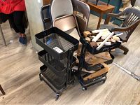 Overview of two black metal rolling carts and four folding chairs with scrap wood in one cart.