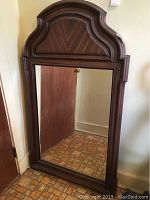 Full view of the wall mirror showing rectangular mirror surface and the molded plastic frame designed to simulate wood grain and classic shape.