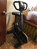 Side angle view of the Vitamaster 62C exercise bike showing padded seat, dual action handlebars, and flywheel.