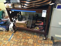 Front view of vintage wooden TV cart filled with various items showing structure and condition.