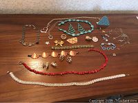 Overview of all jewelry items laid out on wooden surface showing various necklaces, bracelets, pendants, pins, earrings, and cufflinks.