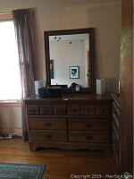 Full frontal view of wooden dresser with framed mirror, showing dresser top and mirror reflecting wall behind.