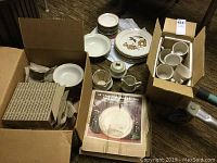 Wide view of boxed and stacked stoneware set, items include plates, cups, and serving pieces mostly packed in cardboard boxes.