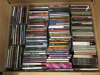 Box full of music CDs tightly packed and stacked with visible spines showing various artist names and album titles.