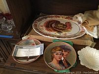 Photo showing a large turkey platter behind two Norman Rockwell illustrated Knowles plates and a white Lenox candy dish.