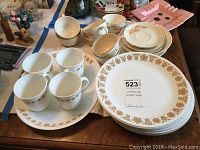 Corning Ware Golden Wheat dishes spread on table showing plates, cups, saucers, and bowl with gold wheat pattern and minor wear at edges.