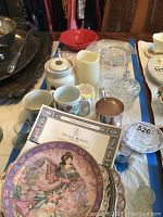Table display showing the Royal Doulton Orchid Maiden dish with certificate, various glassware including aperitif glasses, coffee mugs, candy dishes and other small items.
