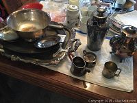 Silverplate platters, bowl, small creamers, baby cup, shaker, teapot on display on table with cloth.
