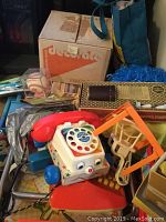 Overall view of assorted toy items including vintage Fisher-Price toy phone, doll furniture, cages, and boxes.