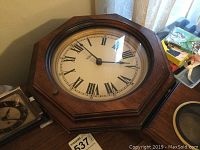 Rusch electric clock with broken lens in wooden octagonal frame showing large white clock face with black Roman numerals