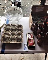 Glass punch bowl, small glass cups on tray, ceramic tiki highball glasses, sealed Marilyn Monroe playing cards on table