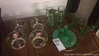 Photo of green glassware including goblets, pitcher, jug, decanter, and saucer alongside handpainted flamingo bowls on a wooden surface.
