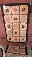 Full view of one hooked rug hanging, showing full pattern of floral blocks and smaller floral/geometric blocks with dark border.