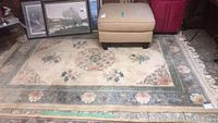 Full view of beige rectangular area rug with floral designs and bordered edges, measuring roughly 8.3 by 5.3 feet, showing it laid out on floor under furniture.