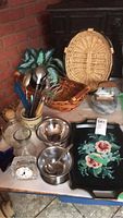 Overall view of kitchen goods including serving utensils, colander, baskets, hand painted tray, and glassware.