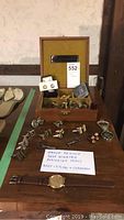 Wide shot of wooden box and table displaying watch, cufflinks, pins, belt buckle, keys