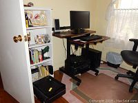 Wide view of computer desk with Dell monitor, keyboard, mouse, and tower computer underneath next to shelving unit.