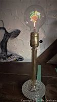 Photo of the lamp with the flamingo filament bulb unlit showing the clear dimple glass base and brass stand.