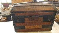 Front view of antique steamer trunk showing wood slats, metal latches, and embossed tin metal central panels.
