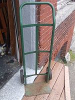 Front angle showing entire hand truck with green steel frame, base plate, and solid rubber tires.