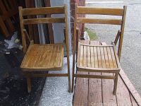Full view of two vintage wooden folding chairs standing side by side showing their slatted seats and backrests with natural wood finish.
