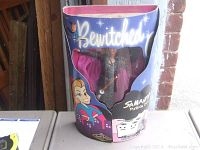 Front view of doll in original packaging showing Bewitched logo, artwork of Samantha, and the doll wearing black sparkly outfit with pink cape and wand.