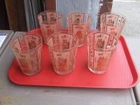 Six mid-century cocktail glasses with orange-gold Geisha designs on a red tray